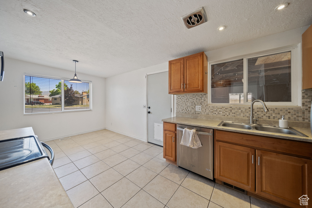 Kitchen featuring dishwasher, brown cabinets, light countertops, backsplash, and pendant lighting