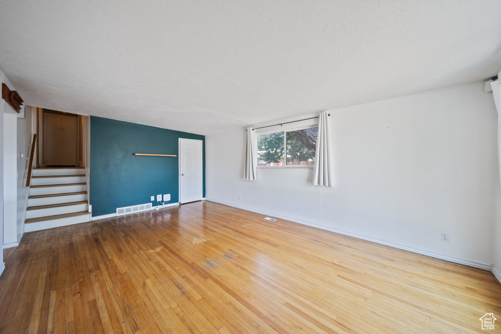 Unfurnished living room with stairs, wood-type flooring, and a textured ceiling