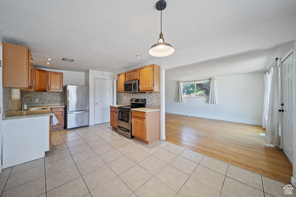 Kitchen with appliances with stainless steel finishes, light tile patterned floors, tasteful backsplash, light countertops, and hanging light fixtures