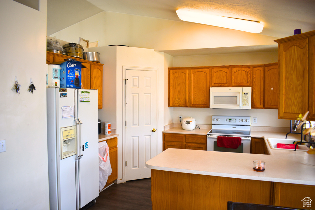Kitchen featuring white appliances, light countertops, a peninsula, and brown cabinetry