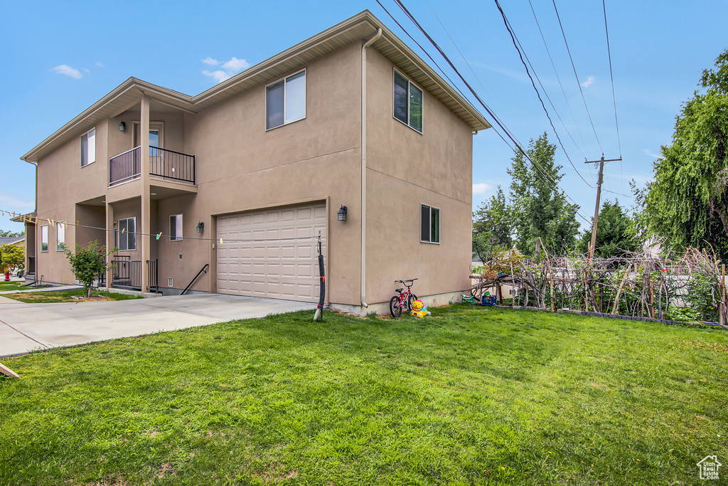 View of side of home with an attached garage, stucco siding, concrete driveway, and a yard