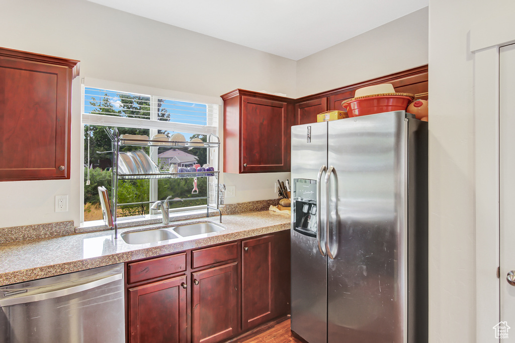 Kitchen with appliances with stainless steel finishes, dark brown cabinets, light stone counters, and wood finished floors
