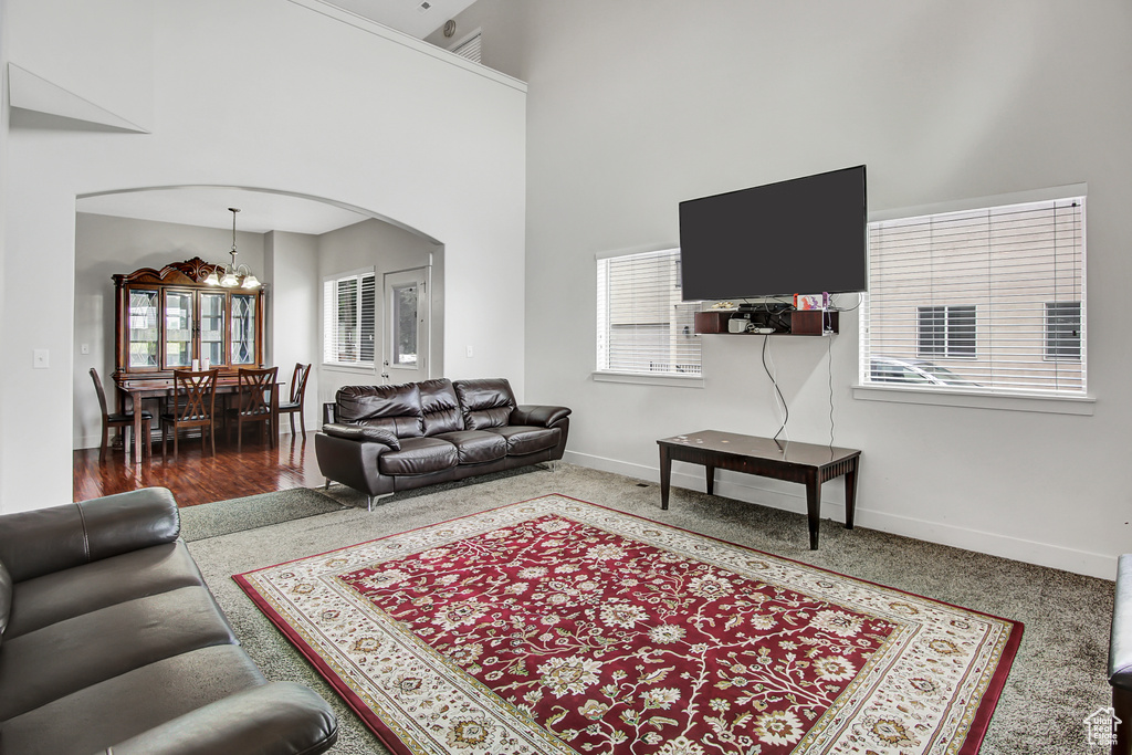 Carpeted living room featuring arched walkways, a chandelier, and a high ceiling