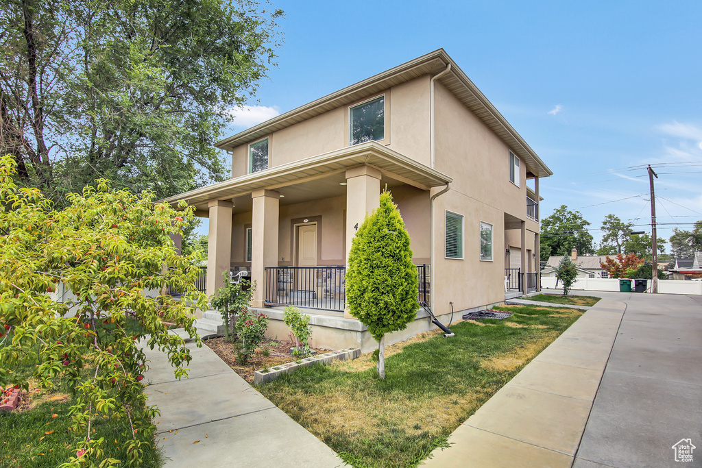 View of front of property with covered porch, stucco siding, and a front yard