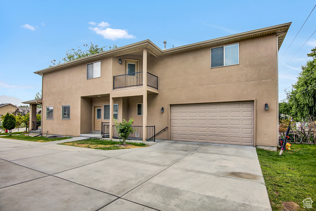 Townhome / multi-family property with a balcony, a garage, stucco siding, and driveway