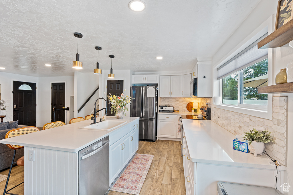Kitchen with appliances with stainless steel finishes, a kitchen bar, light countertops, decorative backsplash, and light wood finished floors