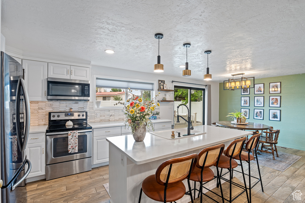Kitchen with stainless steel appliances, light wood finished floors, light countertops, and a textured ceiling