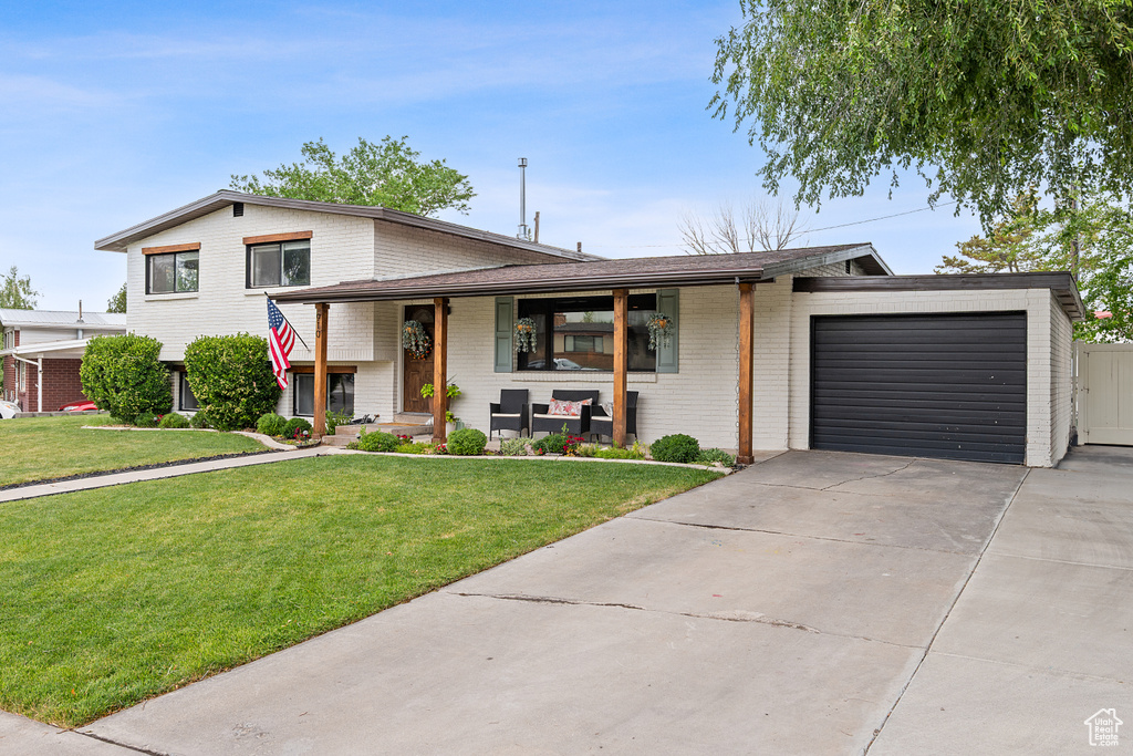 Tri-level home featuring a garage, brick siding, concrete driveway, and a front yard