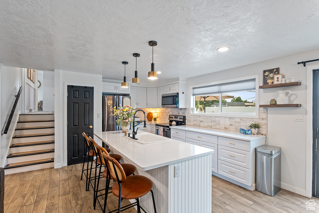 Kitchen featuring appliances with stainless steel finishes, a textured ceiling, a kitchen bar, light wood-style flooring, and backsplash