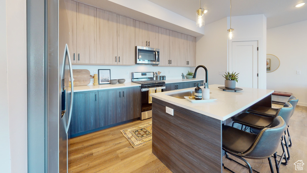 Kitchen with stainless steel appliances, a breakfast bar, light countertops, light wood-type flooring, and a center island with sink