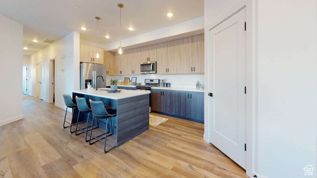 Kitchen with stainless steel appliances, light countertops, a breakfast bar, light brown cabinets, and light wood finished floors
