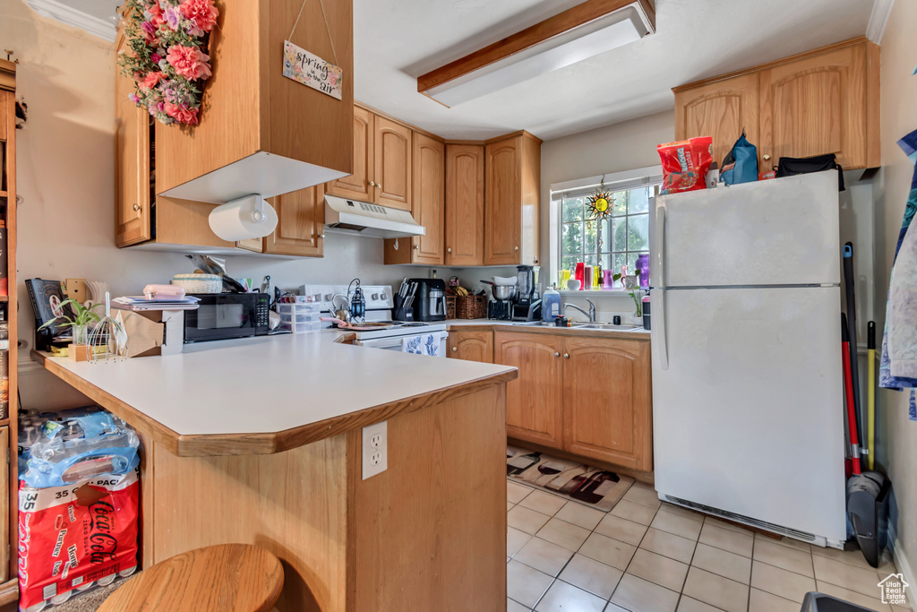 Kitchen with white appliances, under cabinet range hood, a peninsula, light tile patterned floors, and light countertops