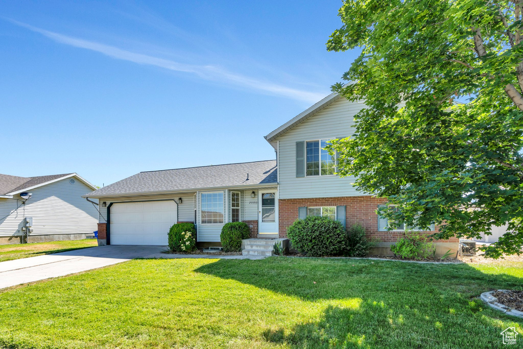 Tri-level home featuring a garage, brick siding, concrete driveway, and a front yard