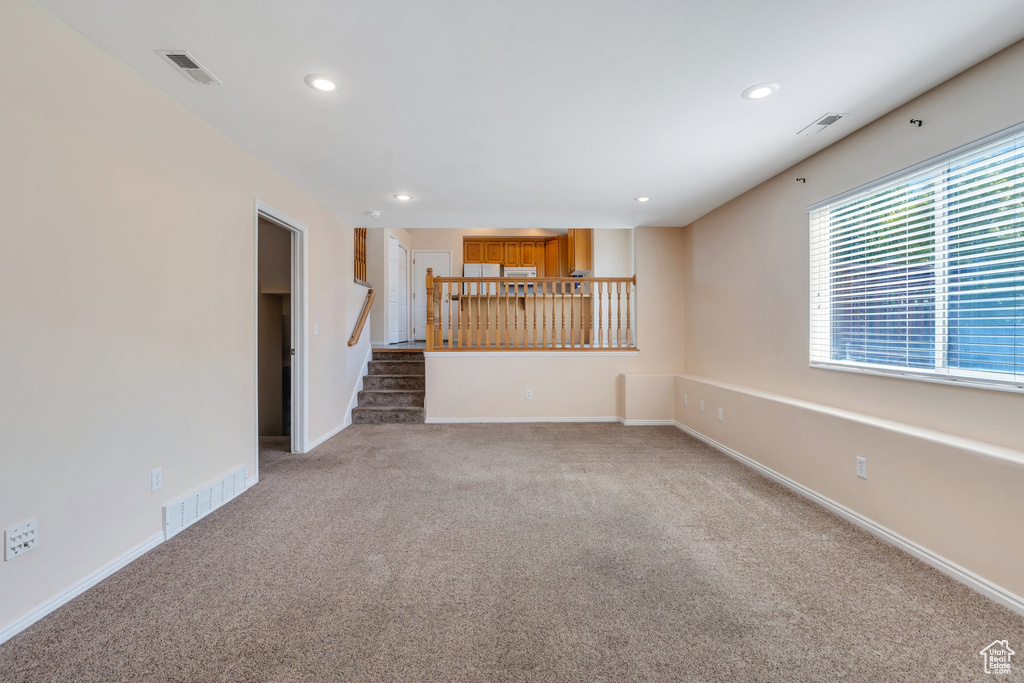 Unfurnished living room featuring carpet floors, recessed lighting, and stairway