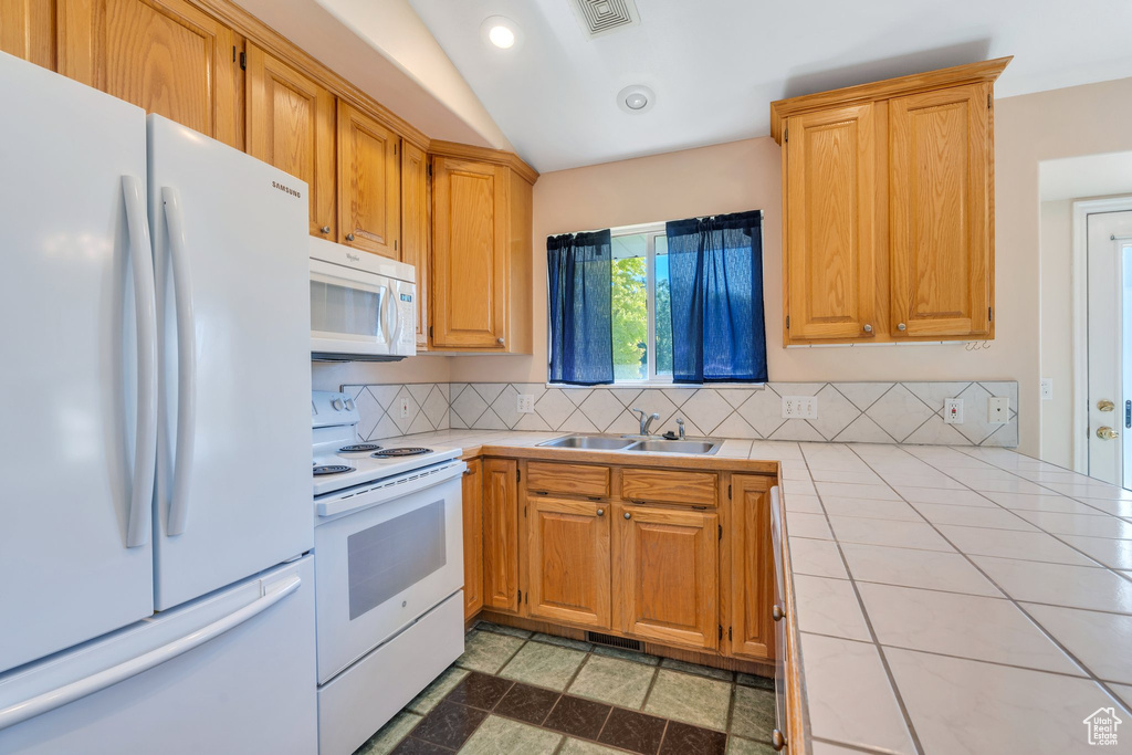 Kitchen with white appliances, tile countertops, backsplash, recessed lighting, and lofted ceiling