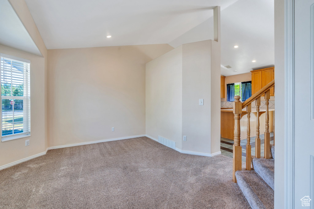 Empty room featuring vaulted ceiling, carpet floors, stairs, plenty of natural light, and recessed lighting