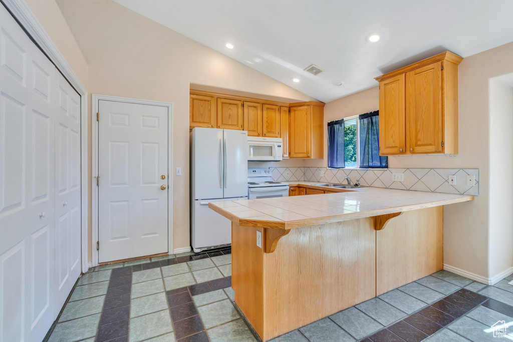 Kitchen featuring white appliances, a peninsula, decorative backsplash, lofted ceiling, and a breakfast bar area