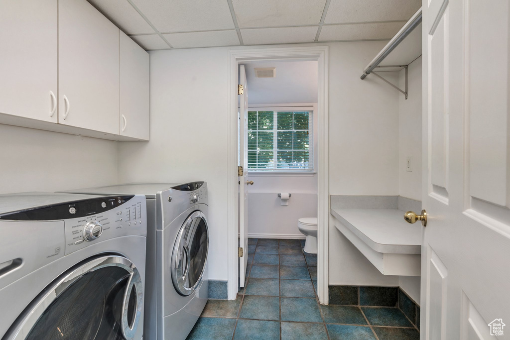 Laundry area with washer and clothes dryer, dark tile patterned flooring, and cabinet space
