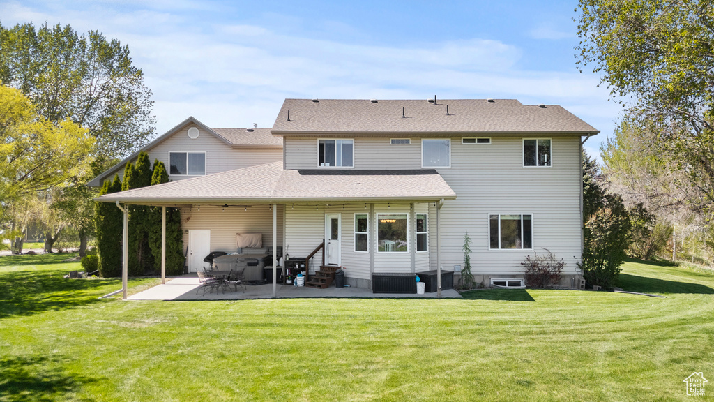 Rear view of house featuring entry steps, a patio area, a lawn, and roof with shingles