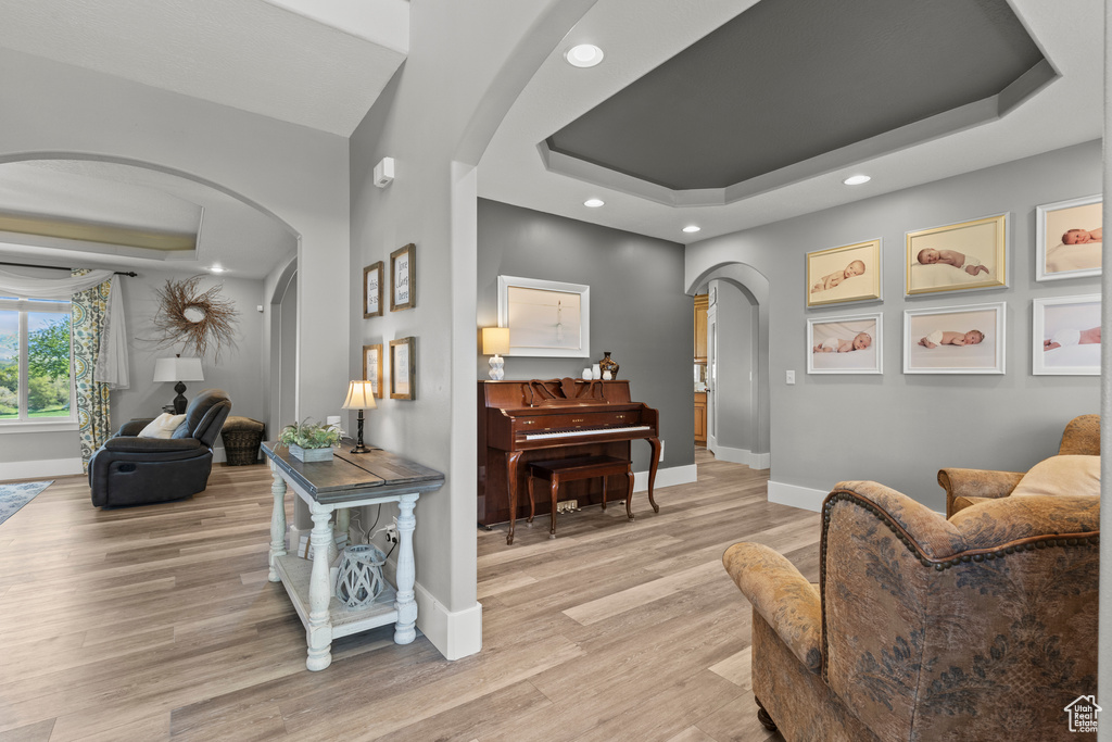 Living room with arched walkways, a raised ceiling, light wood-style floors, and recessed lighting