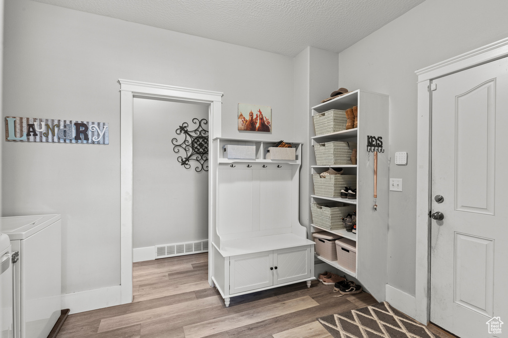Mudroom featuring washing machine and clothes dryer, wood finished floors, and a textured ceiling