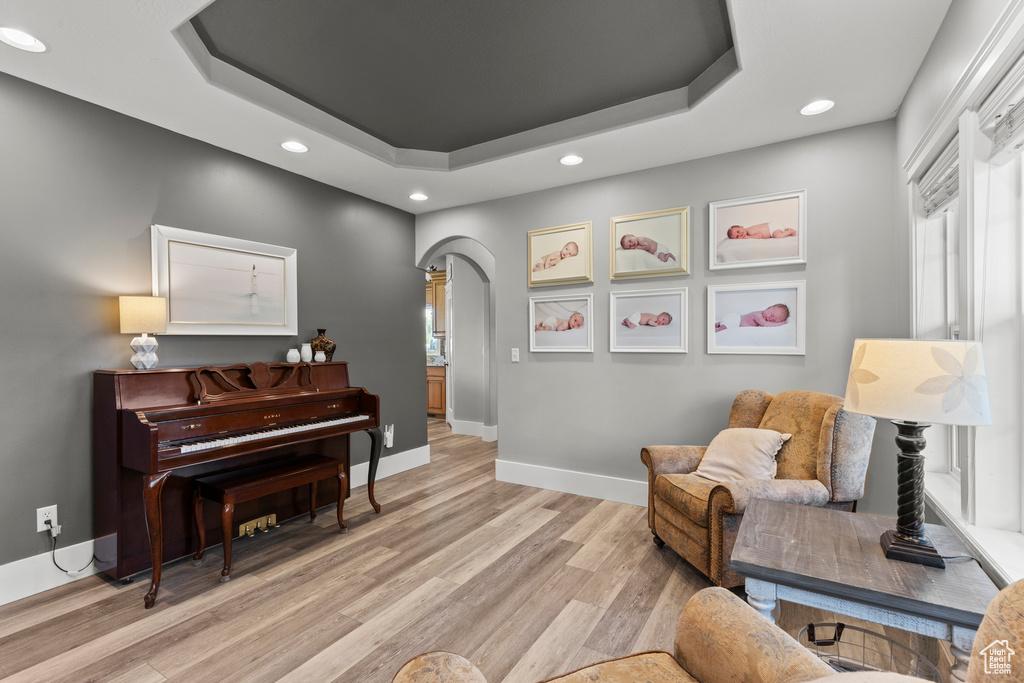 Sitting room featuring a raised ceiling, arched walkways, recessed lighting, and light wood finished floors