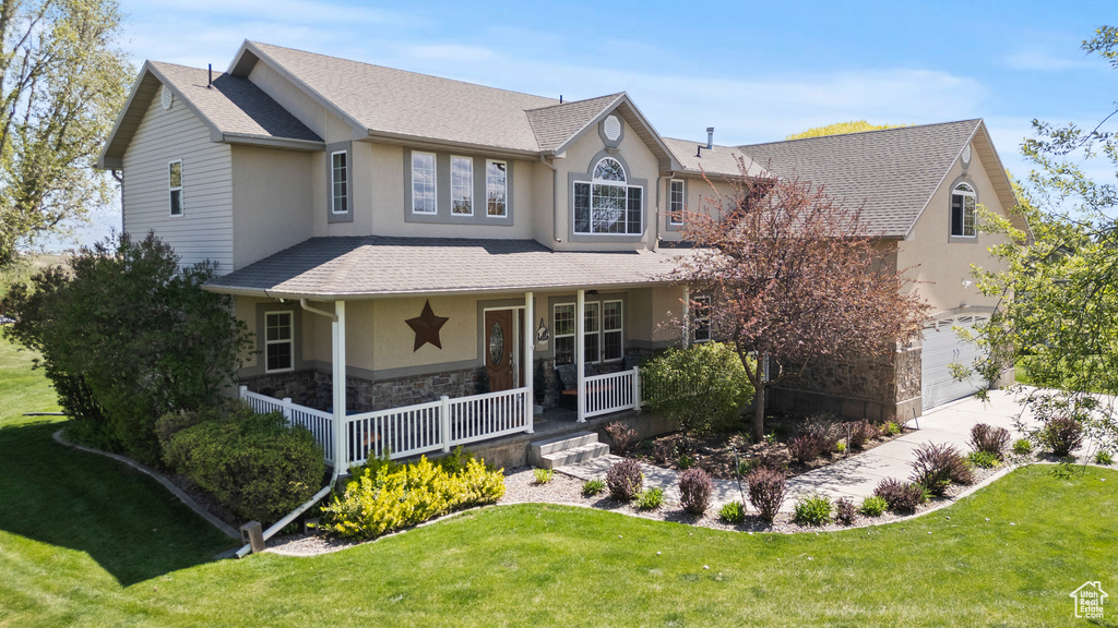 View of front of house with covered porch, stone siding, an attached garage, stucco siding, and a front yard