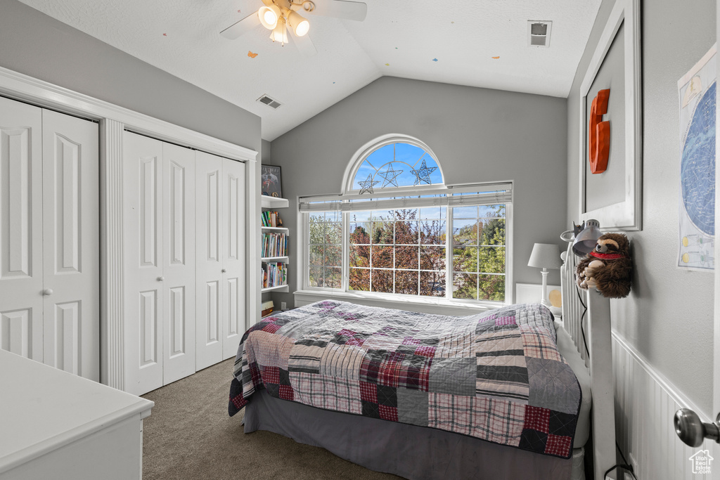 Carpeted bedroom with vaulted ceiling, two closets, and a ceiling fan
