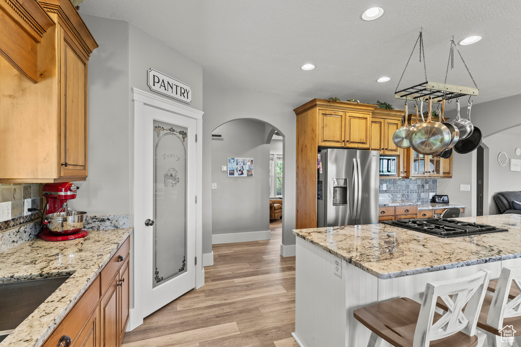 Kitchen with stainless steel refrigerator with ice dispenser, arched walkways, a breakfast bar area, backsplash, and light stone countertops