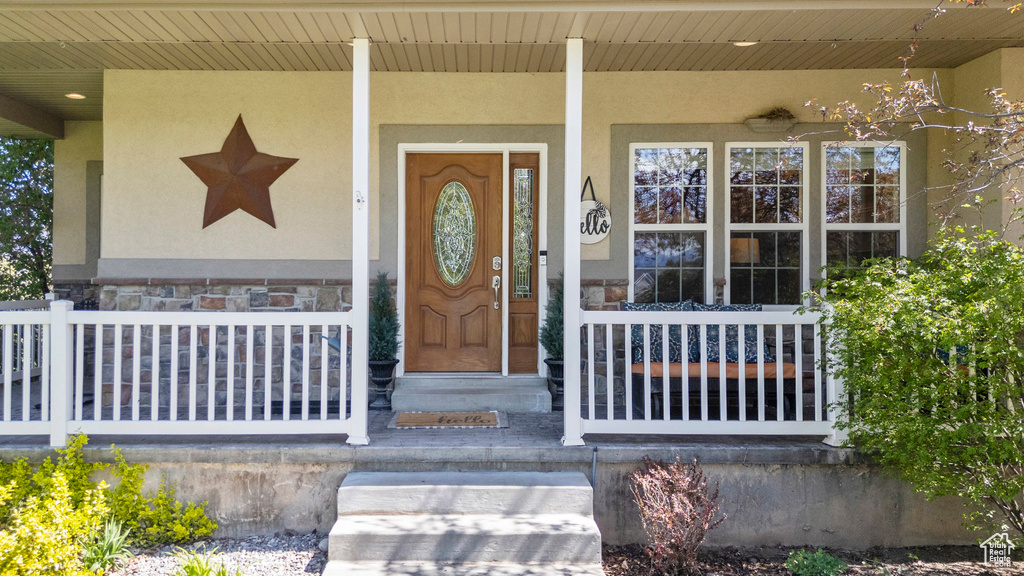 Doorway to property featuring a porch, stucco siding, and stone siding