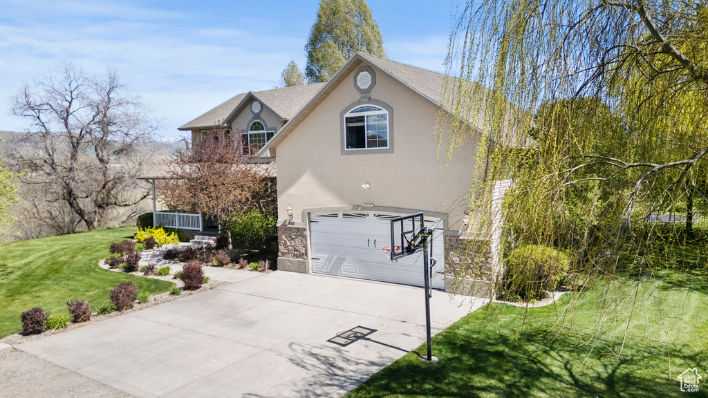 View of front of home featuring concrete driveway, stucco siding, an attached garage, a front lawn, and stone siding