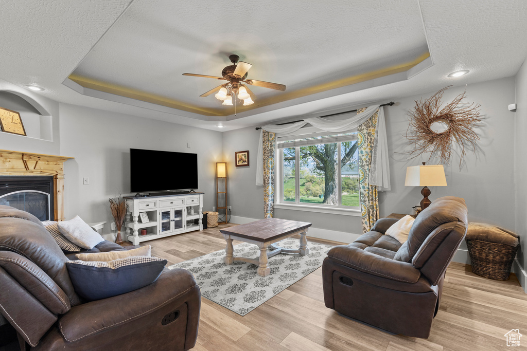 Living area featuring a tray ceiling, ceiling fan, light wood finished floors, a glass covered fireplace, and recessed lighting