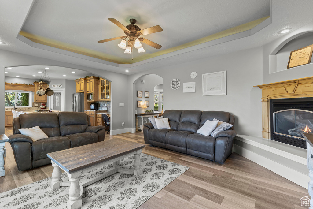 Living room with arched walkways, a raised ceiling, a glass covered fireplace, light wood finished floors, and recessed lighting