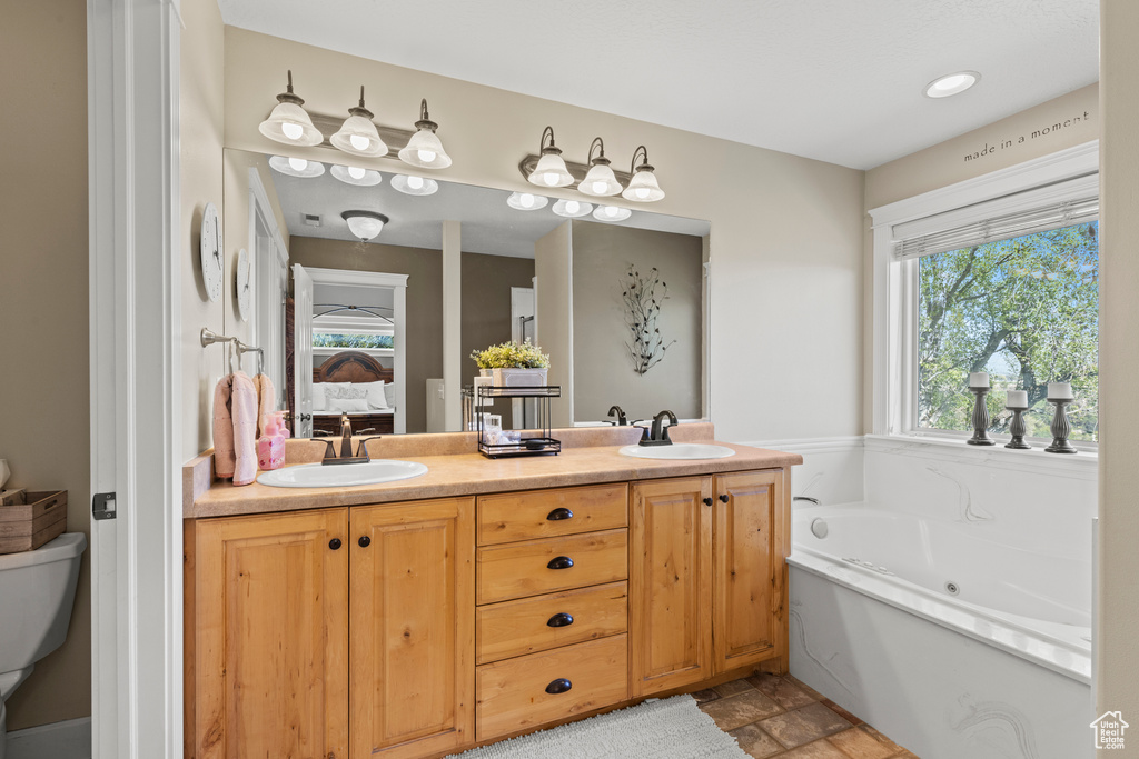Ensuite bathroom with a whirlpool tub, double vanity, and stone finish flooring