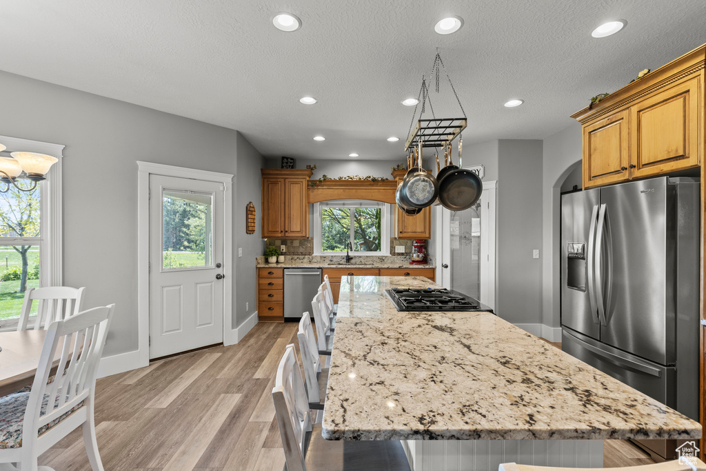 Kitchen with stainless steel appliances, light wood-type flooring, recessed lighting, light stone counters, and a center island