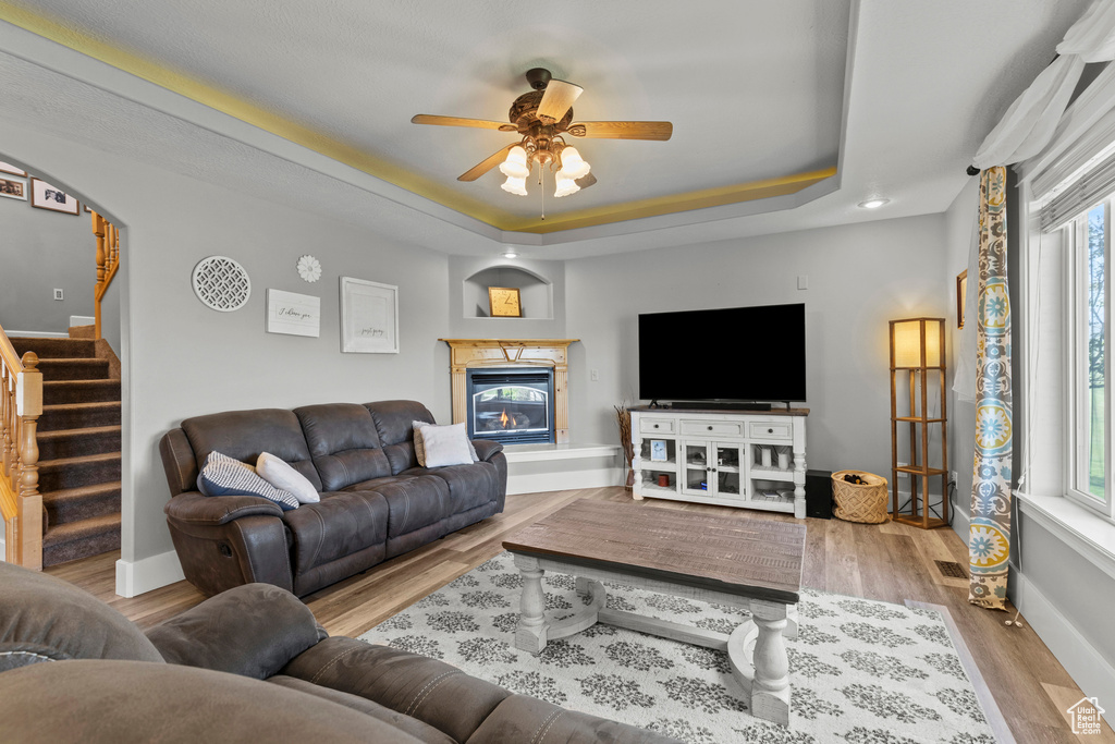 Living room with a raised ceiling, a ceiling fan, stairs, and plenty of natural light