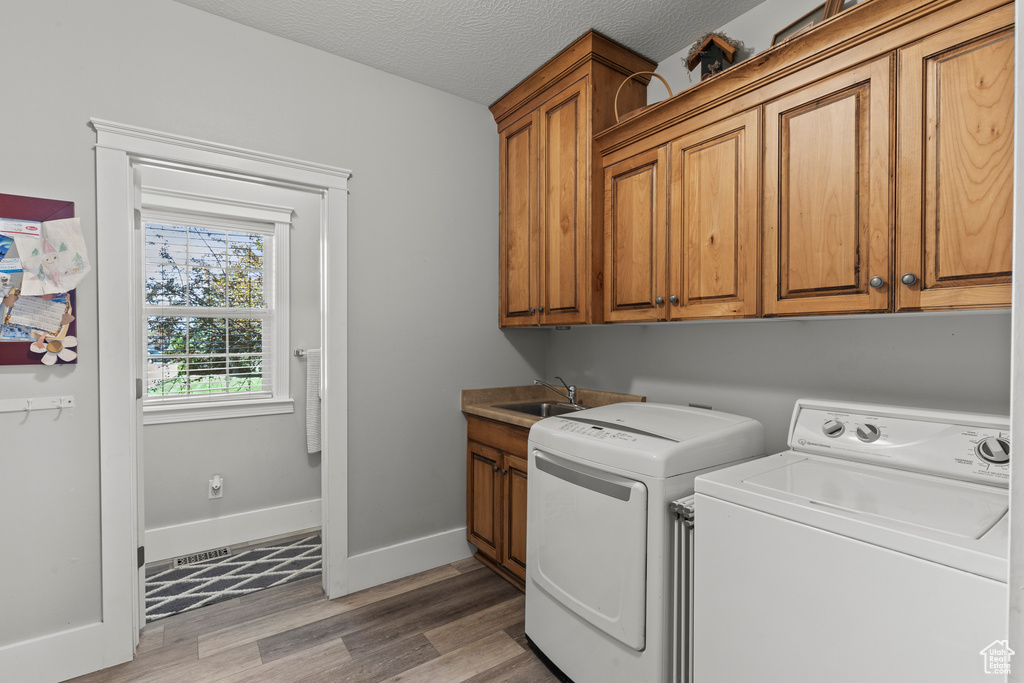 Washroom with washer and clothes dryer, cabinet space, light wood-style flooring, and a textured ceiling