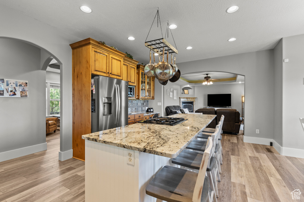 Kitchen featuring appliances with stainless steel finishes, arched walkways, ceiling fan, brown cabinetry, and a kitchen island