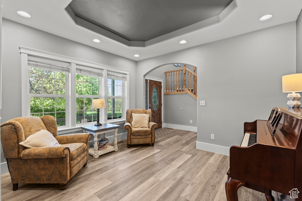 Living area featuring a tray ceiling, light wood-style flooring, recessed lighting, and arched walkways
