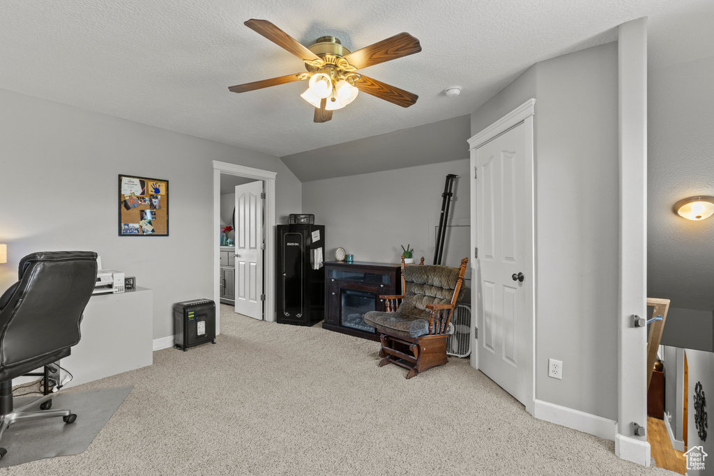 Carpeted home office featuring a ceiling fan and a glass covered fireplace
