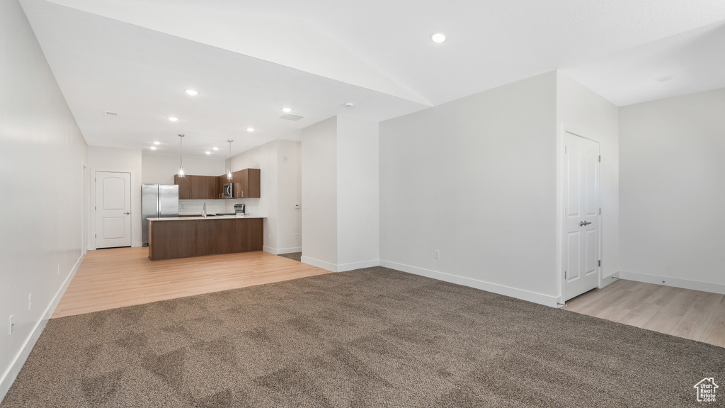 Unfurnished living room with light colored carpet, light wood finished floors, recessed lighting, and vaulted ceiling