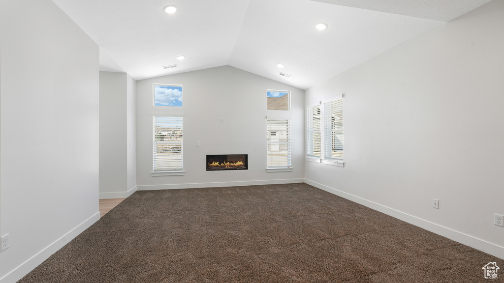 Unfurnished living room featuring carpet floors, healthy amount of natural light, vaulted ceiling, a glass covered fireplace, and recessed lighting