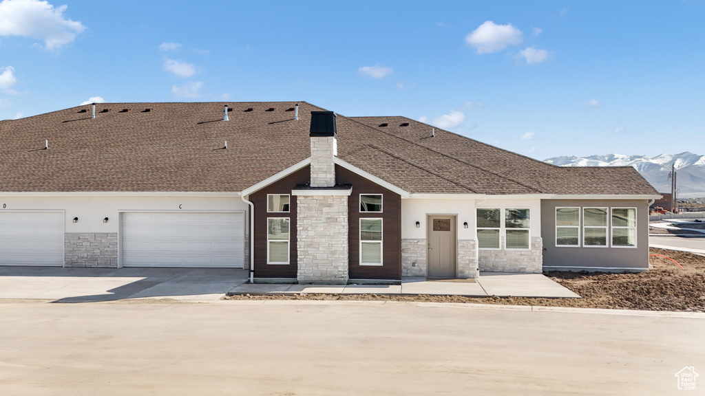 View of front facade featuring stone siding, a garage, driveway, a shingled roof, and a mountain view