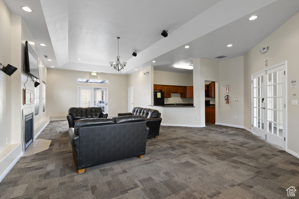 Living room featuring dark colored carpet, recessed lighting, a tray ceiling, a chandelier, and a fireplace with flush hearth