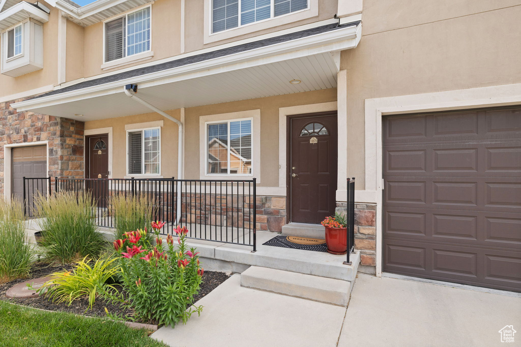 Doorway to property featuring stone siding, covered porch, stucco siding, and driveway
