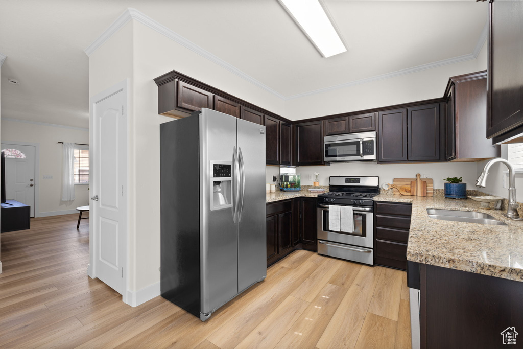 Kitchen with appliances with stainless steel finishes, light stone counters, light wood finished floors, dark brown cabinets, and crown molding