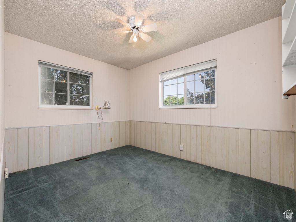 Spare room featuring wood walls, carpet, a wainscoted wall, a textured ceiling, and ceiling fan