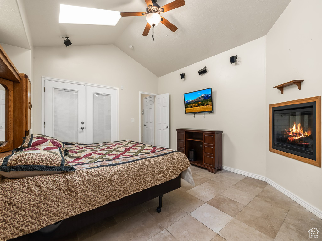 Bedroom featuring high vaulted ceiling, a glass covered fireplace, french doors, a skylight, and ceiling fan
