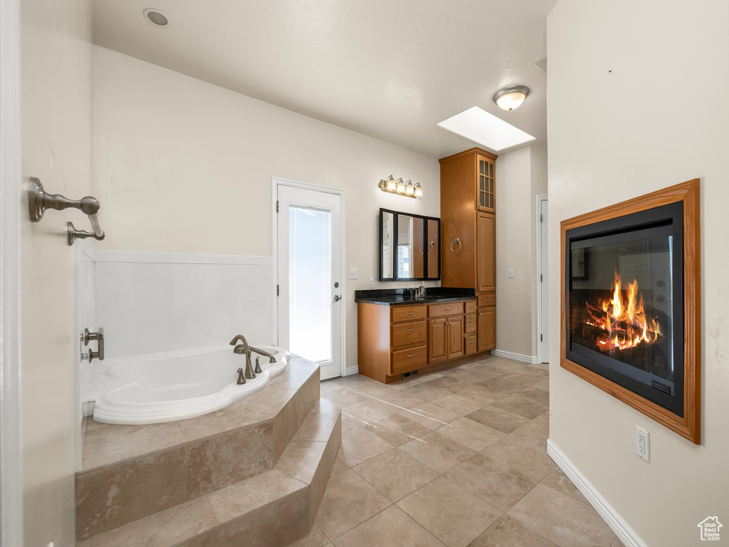 Bathroom with vanity, a garden tub, a glass covered fireplace, and tile patterned flooring