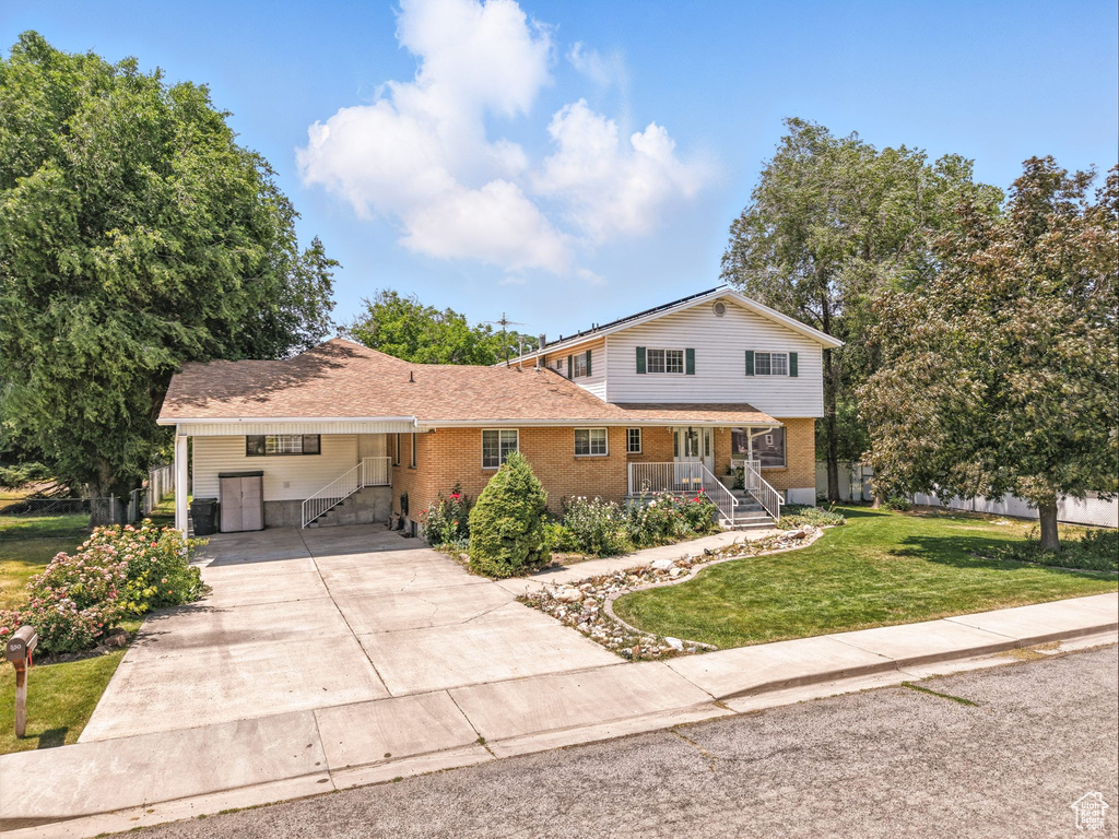 View of front of home with a front yard, brick siding, concrete driveway, and an attached carport